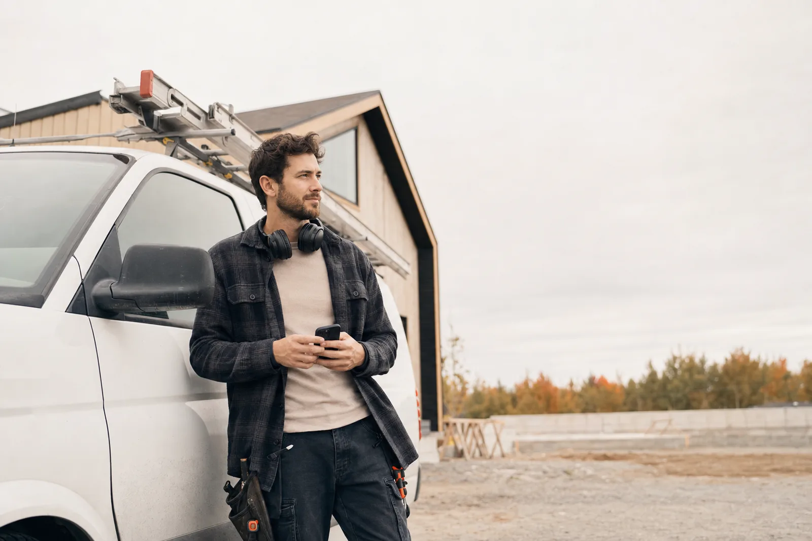 Entrepreneur appuyé sur sa camionnette de travail, cellulaire en main